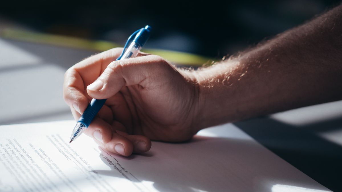 Detalle de una mano escribiendo en un documento con un bolígrafo azul